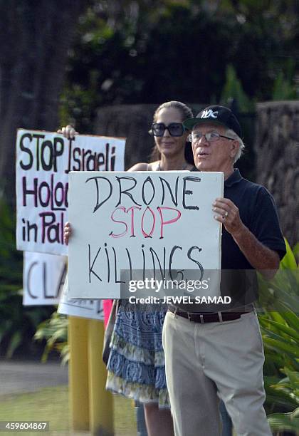 Group of protesters show placards as US President Barack Obama's motorcade arrives at his vacation home in Kailua, Hawaii, on December 28, 2013. The...