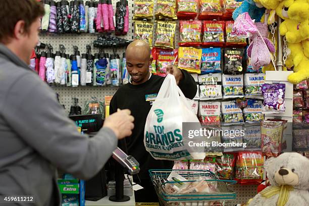 An employee right, passes a customer his purchases inside a plastic carrier bag at the checkout counter inside a Poundland discount store, operated...