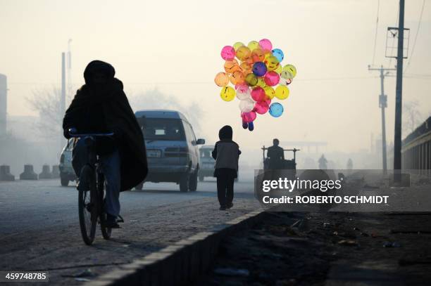 In this photograph taken on December 27 Bashir, an Afghan boy who says he is five years old, holds balloons for sale along a street at dawn in Kabul....