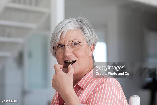 senior woman eating chocolate - eating chocolate stock-fotos und bilder