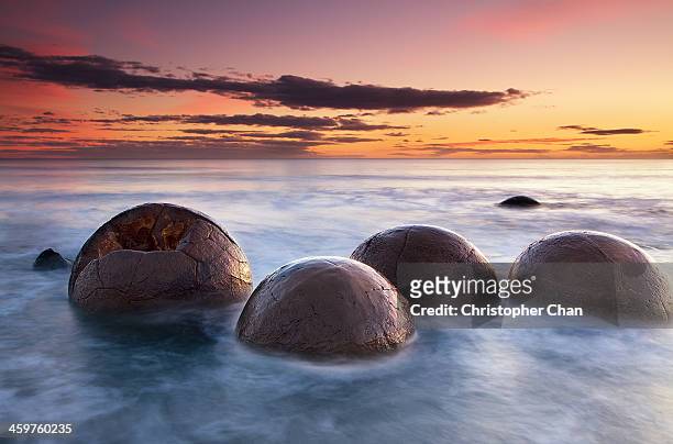 spherical boulders in the sea at sunrise - otago stockfoto's en -beelden