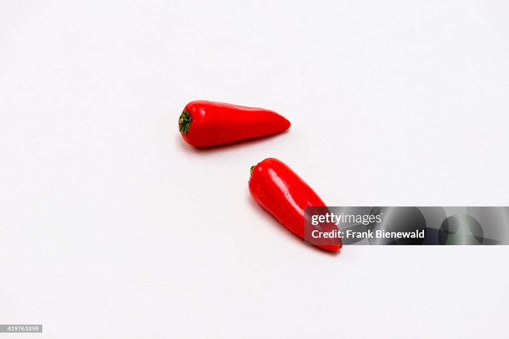 Two red capsicums (Capsicum annuum), displayed on a white...