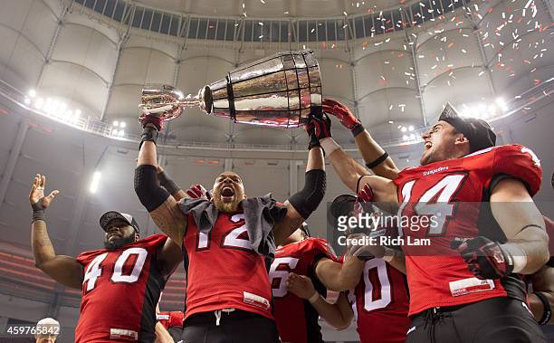 Juwan Simpson of the Calgary Stampeders holds up the Grey Cup with Shawn Lemon and Matt Walter by his side after the Stampeders defeated the Hamilton...