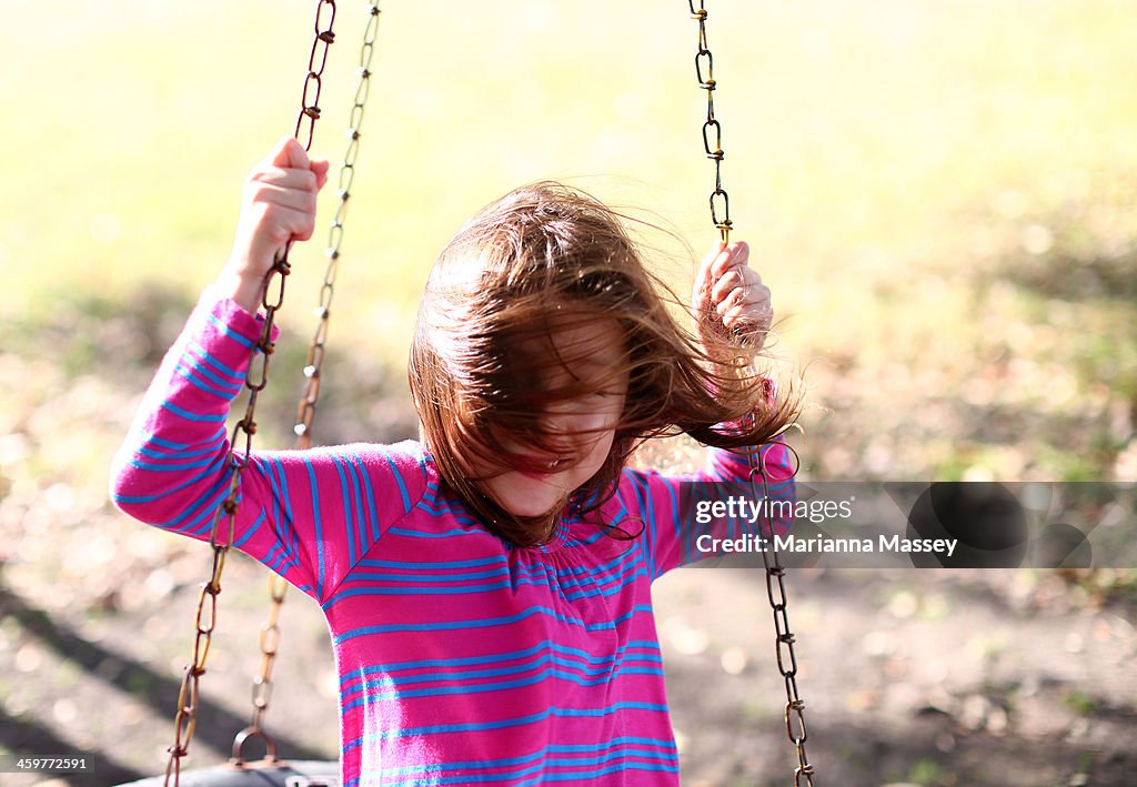 Girl on tire swing with hair blowing in face