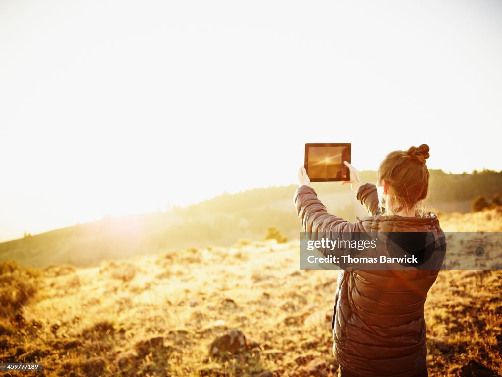 Woman taking photo with digital tablet at sunset