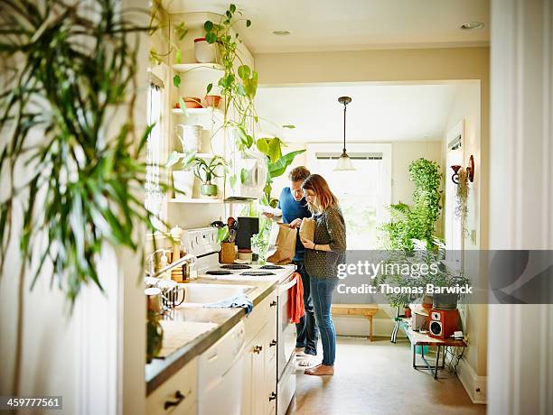 couple unpacking groceries in kitchen of home - couple kitchen stockfoto's en -beelden
