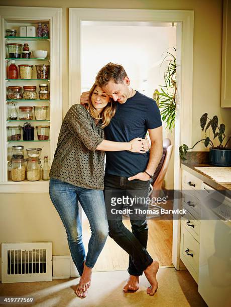 smiling couple embracing in doorway of kitchen - coppia eterosessuale foto e immagini stock
