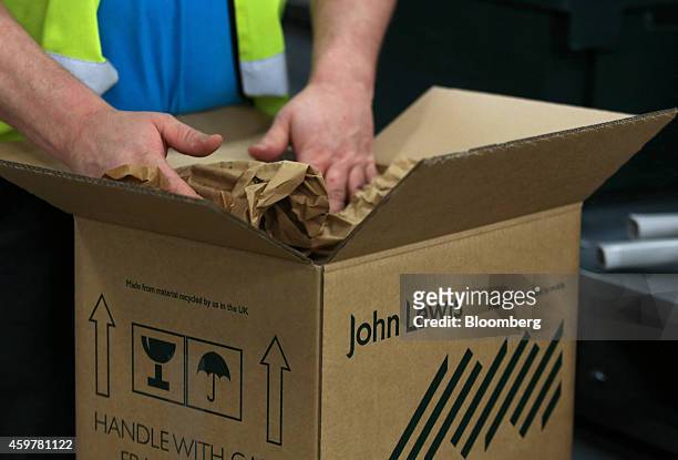 Worker secures a customer's order with paper as he packs a John Lewis branded cardboard box at the John Lewis Plc semi-automated distribution centre...