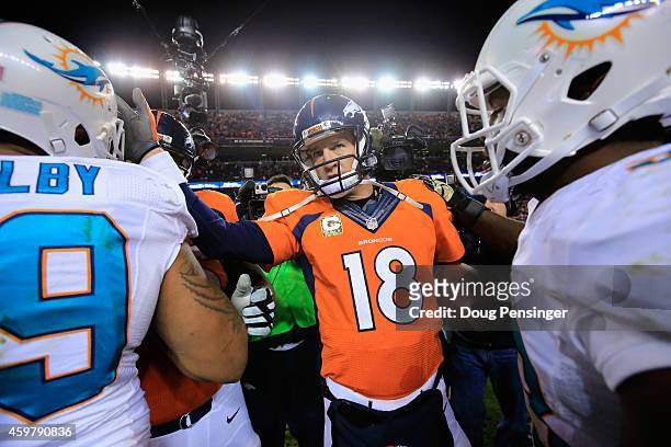 Quarterback Peyton Manning of the Denver Broncos greets defensive end Derrick Shelby and outside linebacker Jelani Jenkins of the Miami Dolphins...