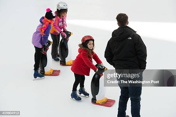 Hannah Spellman of Bethesda, center, holds onto a penguin for balance. People brave the cold weather on the 26th of December to skate at Silver...