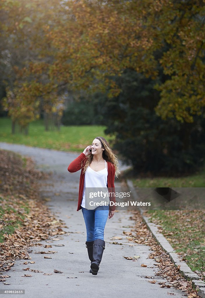 Woman walking through park using mobile phone.