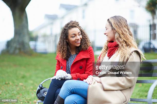 friends talking on park bench. - autumn friends coats stock pictures, royalty-free photos & images