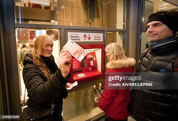 Woman shows a 10 euro note after withdrawing it from a cash machine in Riga on January 1, 2014 as fireworks lit up the capital after midnight,...