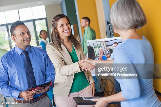 woman shaking hands with professional executive at job fair event - job fair stock pictures, royalty-free photos & images