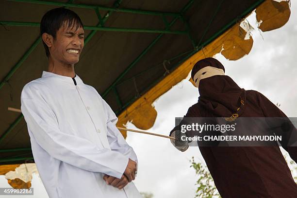 Masked and hooded official canes one of seven Acehmen for gambling in Jantho, Aceh on December 5, 2014. Seven men were caned in Aceh province on...