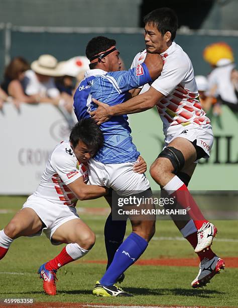 Takashi Suzuki and Ryohei Miki of Japan tackle Lio Loio of Samoa during their rugby match on the first day of the Dubai leg of IRB's Sevens World...