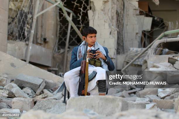 An armed Yemeni youth, loyal to the Shiite Muslim Huthi movement that controls Sanaa, sits amid the rubble on December 5 guarding the damaged house...