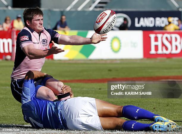 James Johnstone of Scotland passes the ball as he is tackled by Lolo Lui of Samoa during their rugby match on the first day of the Dubai leg of IRB's...