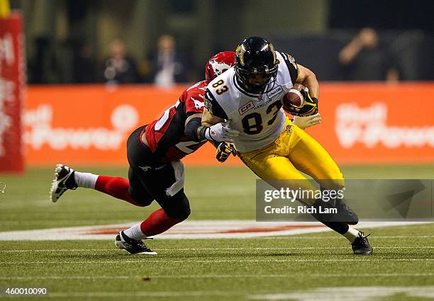 Andy Fantuz of the Hamilton Tiger-Cats is tackled by Keon Raymond of the Calgary Stampeders after making a catch during the 102nd Grey Cup...