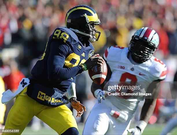 Quarterback Devin Gardner of the Michigan Wolverines runs the ball while avoiding pressure from defensive linemen Noah Spence of the Ohio State...