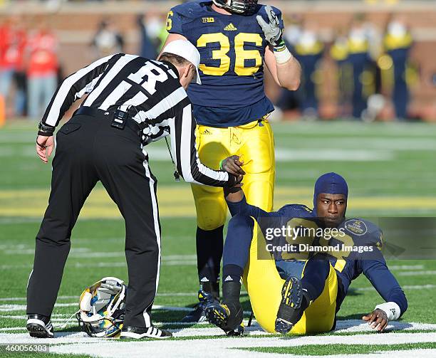 Quarterback Devin Gardner of the Michigan Wolverines is helped up by the referee after being knocked down and losing his helmet during a game against...