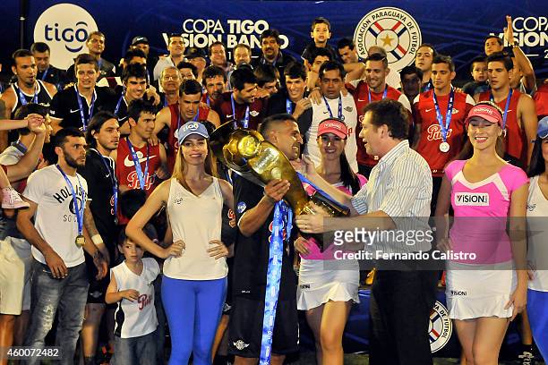 Sergio Aquino of Libertad lifts the trophy to celebrate the championship with teammates after winning a match between Nacional and Libertad as part...