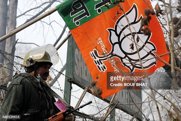 An Indian paramilitary soldier stands guard next to a Bharatiya Janata Party campaign flag during a curfew in Srinagar on December 8, 2014. Prime...