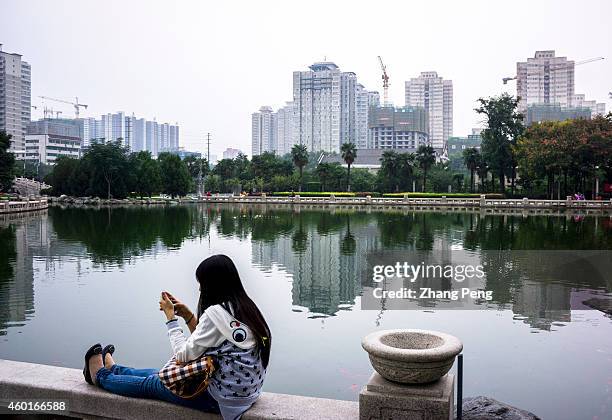 Girl is reading her smart phone in a city park, and residential houses on construction are reflected in the pond. On Dec. 9, 2014The central economic...