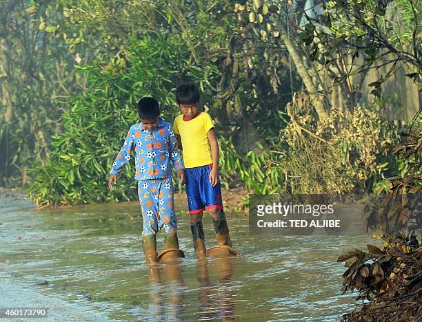 Boy in his pajamas and his friend walk along a mudded street after a river overflowed at the height of Typhoon Hagupit at a village along a highway...