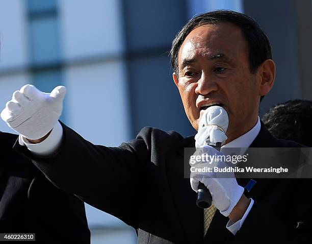 Japan's ruling Liberal Democratic Party Chief Cabinet Secretary Yoshihide Suga speaks to voters from the roof of a campaign bus during his party...