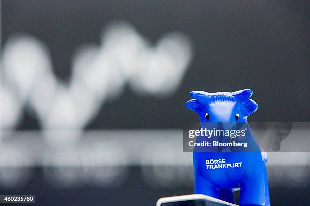 Toy bull figurine is seen as the DAX Index curve is displayed on an electronic board beyond at the Frankfurt Stock Exchange in Frankfurt, Germany, on...