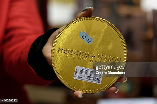 Employee holds a giant gold chocolate coin displayed for sale inside a pop-up store, operated by Fortnum & Mason Plc, during a seasonal Christmas...
