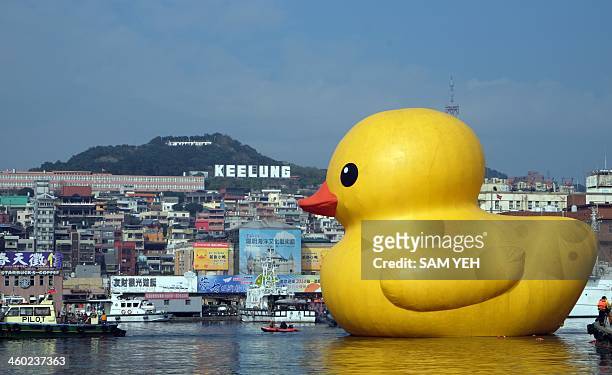 Visitors look at an 18-metre-tall bath toy duck replica created by Dutch artist Florentijn Hofman as it floats its repair in Keelung harbor after...