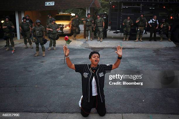 Bloomberg's Best Photos 2014: A demonstrator holding a red rose kneels in front of armed police officers and raises their hands above her head during...