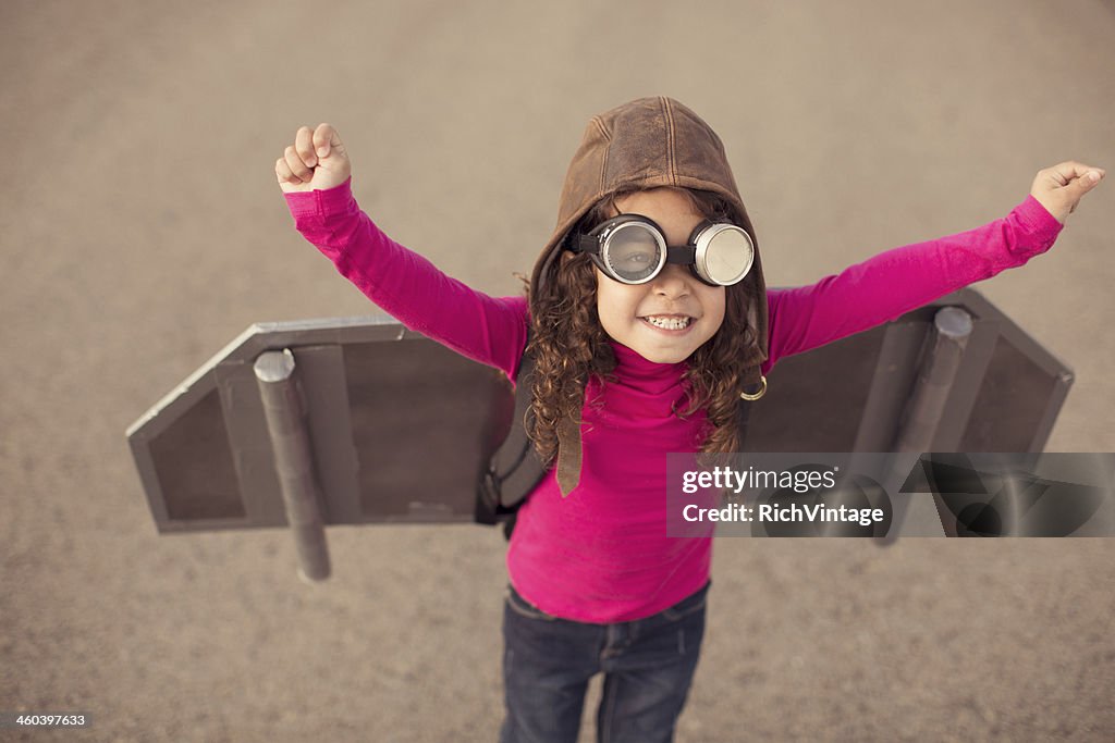 Young girl in pilot gear with toy aircraft wings