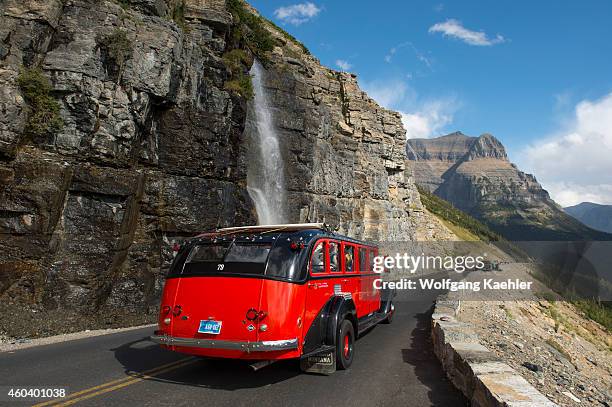 Red tour bus at waterfall coming down next to the Going-to-the-Sun Road near Logan Pass in Glacier National Park, Montana, United States.