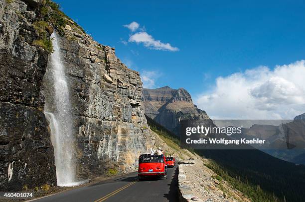 Red tour bus at waterfall coming down next to the Going-to-the-Sun Road near Logan Pass in Glacier National Park, Montana, United States.