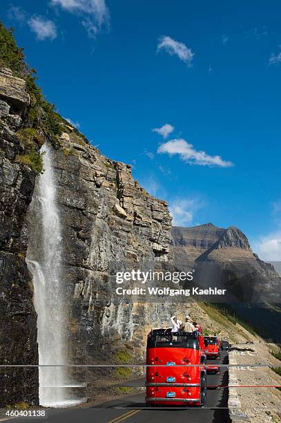 Red tour bus at waterfall coming down next to the Going-to-the-Sun Road near Logan Pass in Glacier National Park, Montana, United States.