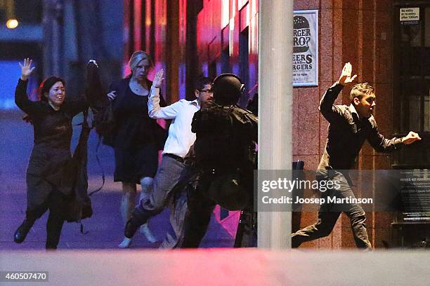 People run with there hands up from the Lindt Cafe, Martin Place during a hostage standoff on December 16, 2014 in Sydney, Australia. Police stormed...