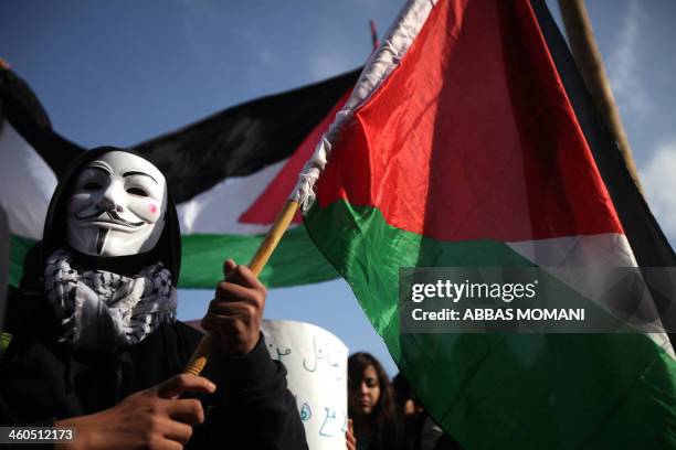 Palestinian wearing a mask of the anonymous movement, holds the national flag during a demonstration in front of the offices of the Palestine...