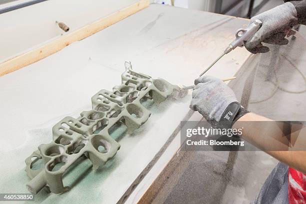 An employee uses a compressed air gun and a brush to clean a sand mold from a water jacket core automotive part at the Voxeljet AG 3-D printing plant...