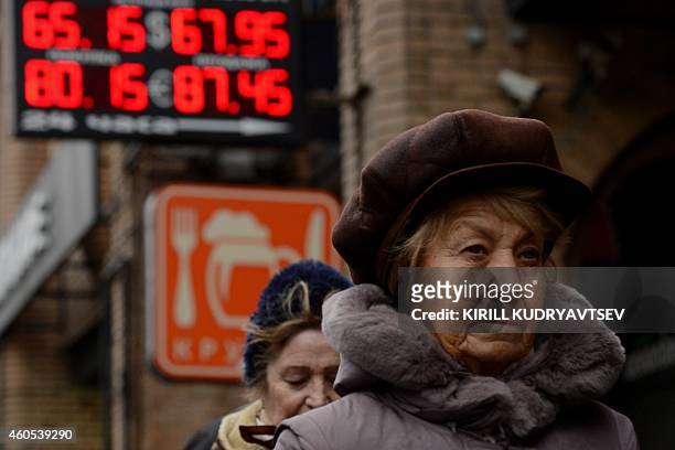 Pedestrians walk past a board listing foreign currency rates against the Russian ruble outside an exchange office in central Moscow on December 16,...