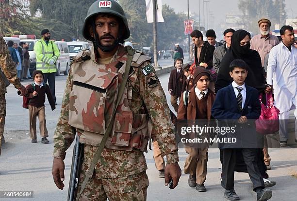 Pakistani soldier stands guard as parents leave with their children near the site of an attack by Taliban gunmen on a school in Peshawar on December...