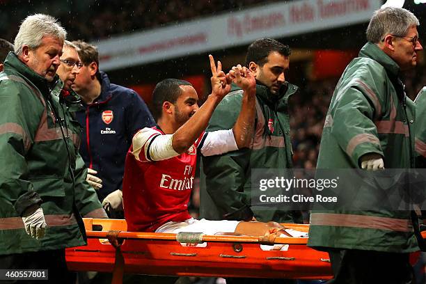 The injured Theo Walcott of Arsenal makes a 2-0 gesture to the Tottenham fans as he is stretchered off the pitch during the Budweiser FA Cup third...