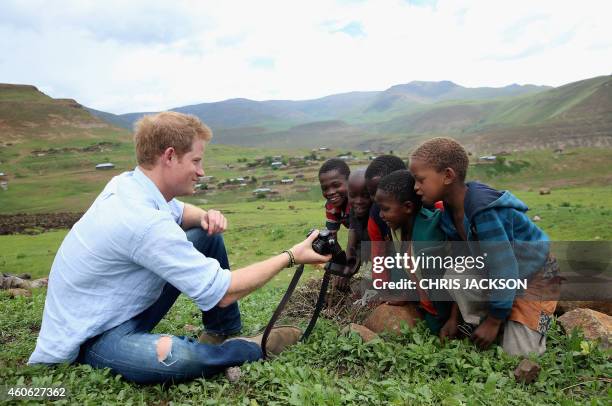 Britain's Prince Harry shows children a photograph he has taken on a camera during a visit to a herd boy night school constructed by Sentebale in...