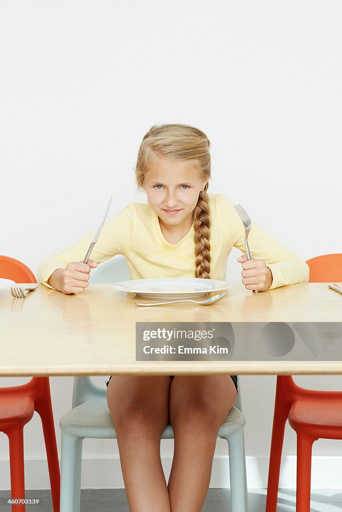 Girl sitting at table with empty plate holding cutlery