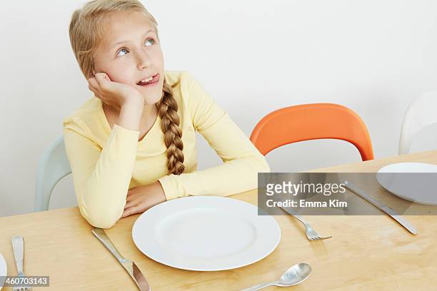 girl sitting at table with empty plate, looking up - children only braided ponytail stock pictures, royalty-free photos & images