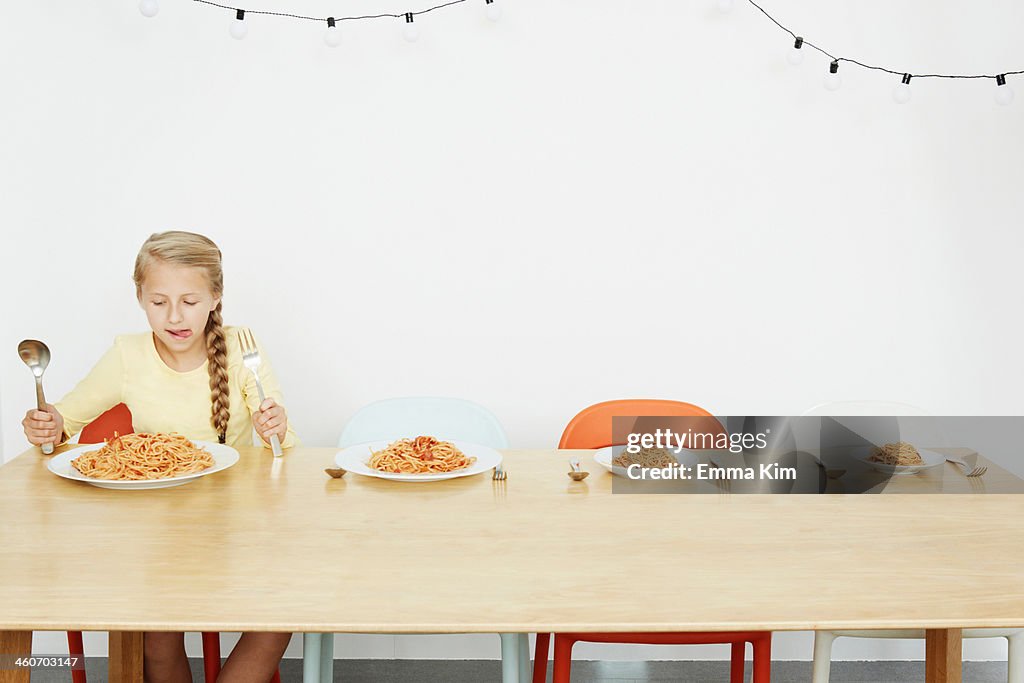 Girl sitting at table with spaghetti and three more plates