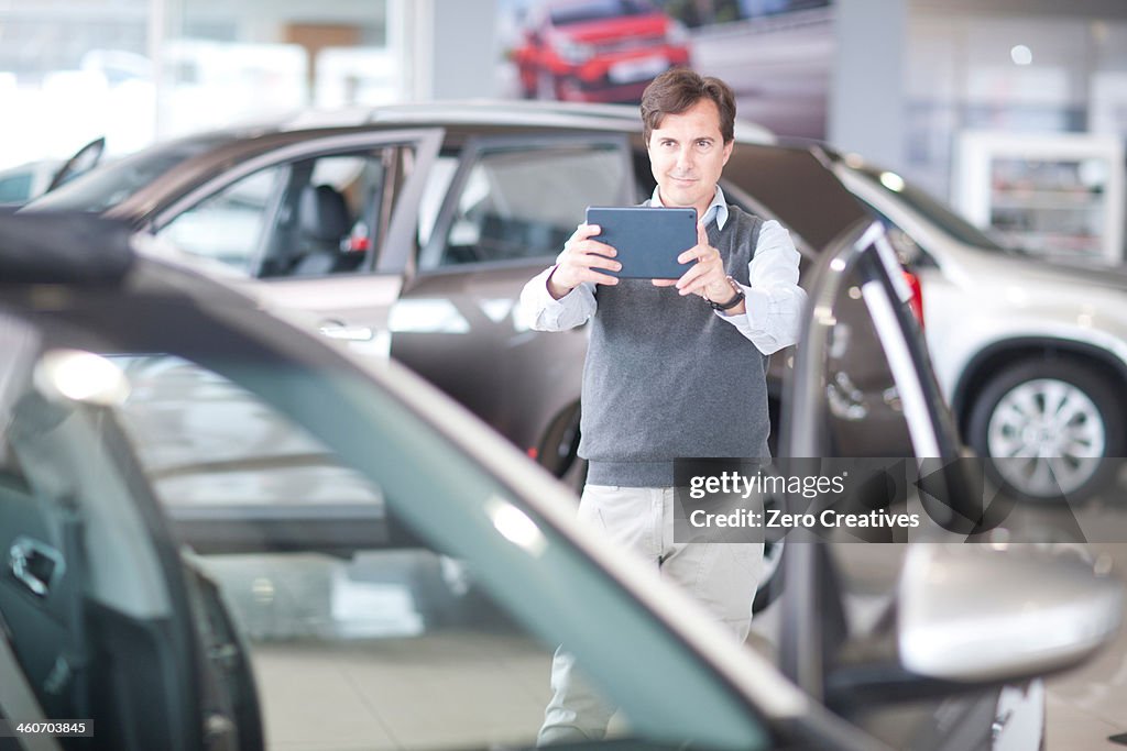 Mid adult man photographing car in showroom
