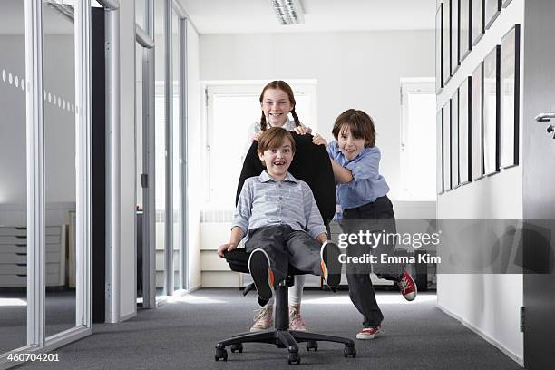 three children playing in office corridor on office chair - facial expression girl office stock pictures, royalty-free photos & images